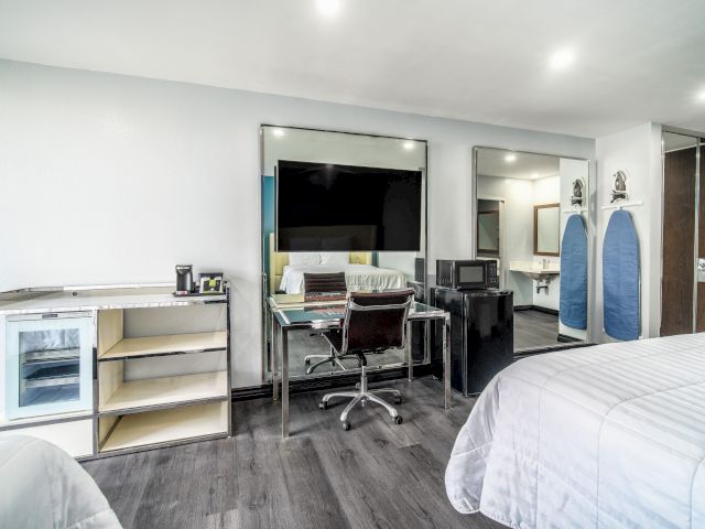 A hotel room with a bed, desk, TV, and mini-fridge.