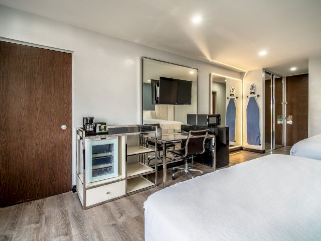 A hotel room with a double bed, desk, mini fridge, and TV.