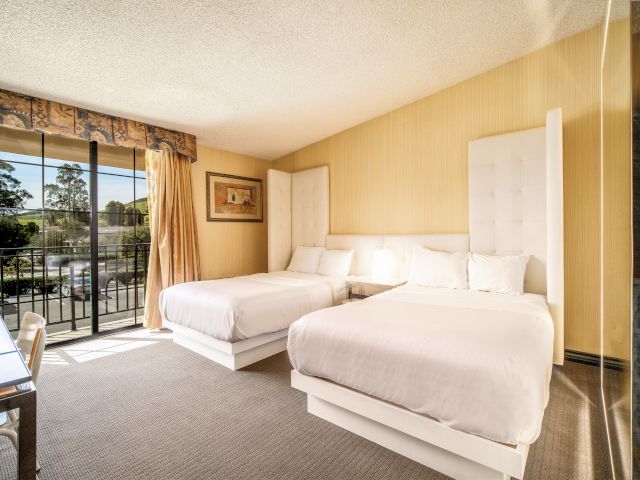 A hotel room with two beds, a balcony, and a view.