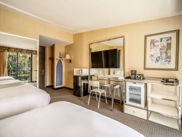 A hotel room with two beds, a desk, a fridge, and a TV