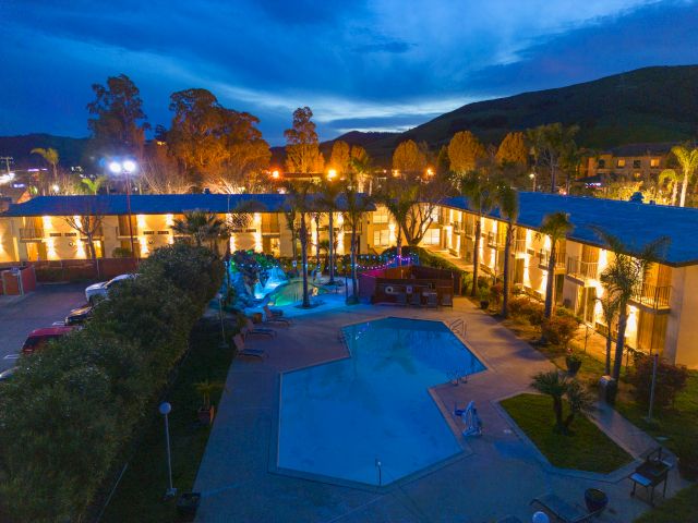 A hotel exterior at dusk with a pool and trees.