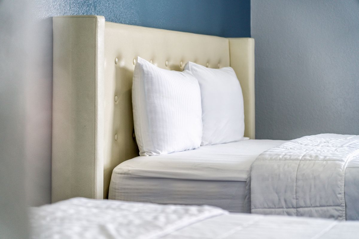 A close-up of a bed with a tufted headboard, white pillows, and white bedding in a room with gray walls and a blue accent wall.
