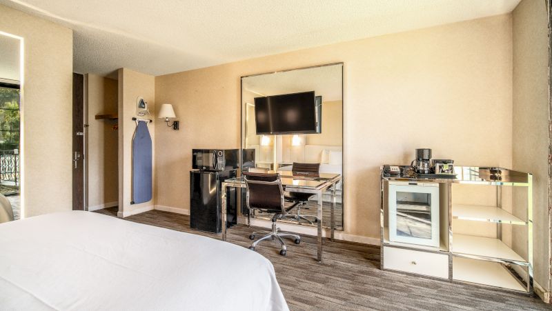 A hotel room with a bed, desk, TV, mini-fridge, and coffee maker.