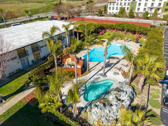 Aerial view of a hotel pool area with palm trees and a parking lot