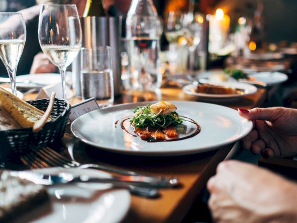 This image shows a dining table with people enjoying a meal, featuring a plated dish, bread, wine glasses, and a cozy ambiance.