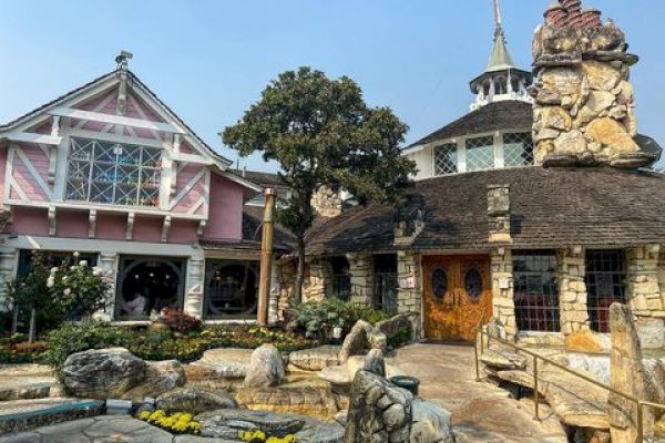 A quaint, fairy-tale-like building with stone and wood architecture, featuring a garden and a pathway leading to the entrance.