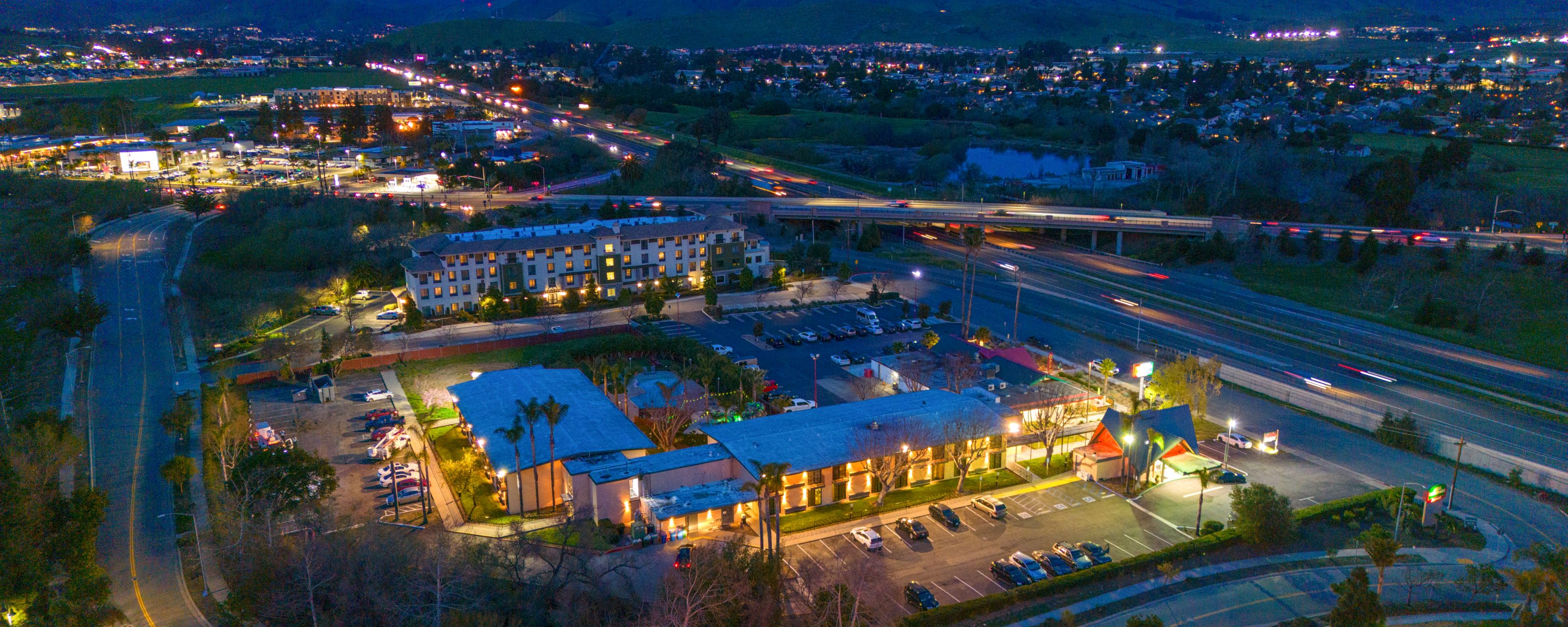 Aerial view of a hotel at night with parking lot and road