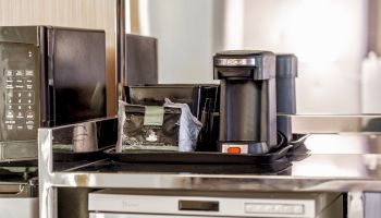 A countertop with a coffee maker, microwave, and assorted coffee supplies beside it, all set up for convenient use.