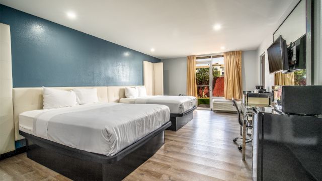 A hotel room with two queen beds, a desk, and a flat-screen TV on the wall.