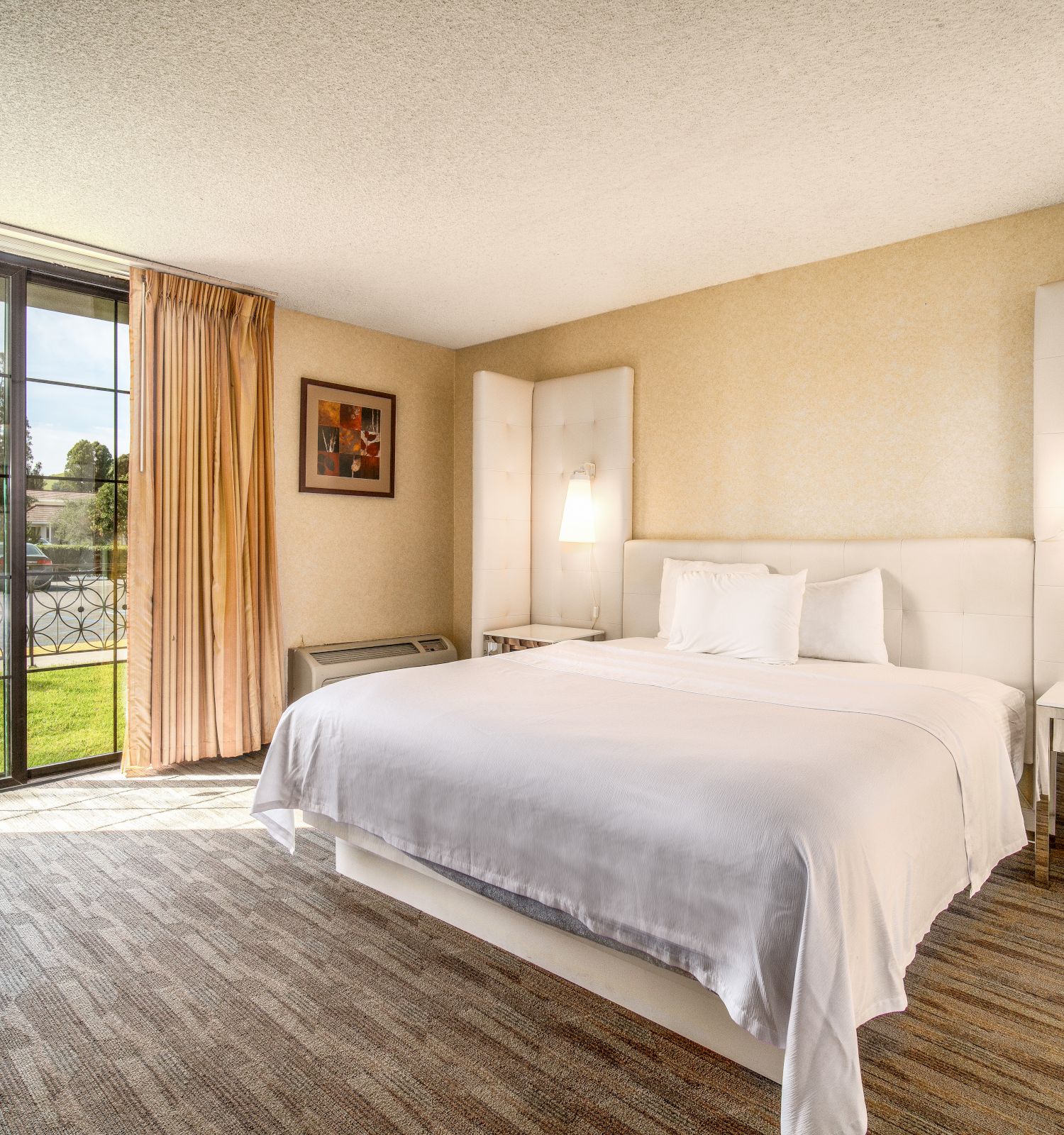 This image depicts a modern hotel room with a king-size bed, desk, large window with curtains, and two nightstands with lamps, featuring a serene ambiance.