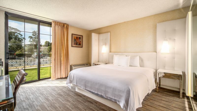 A hotel room with a large bed, desk, and chair in front of a window overlooking a grassy area.